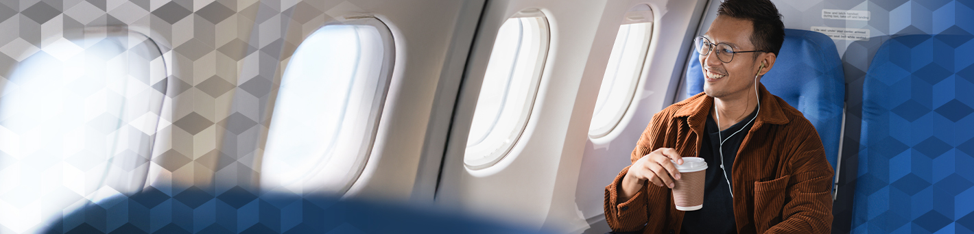 Man sitting in a luxury aircraft with a coffee and looking out the window whist smiling