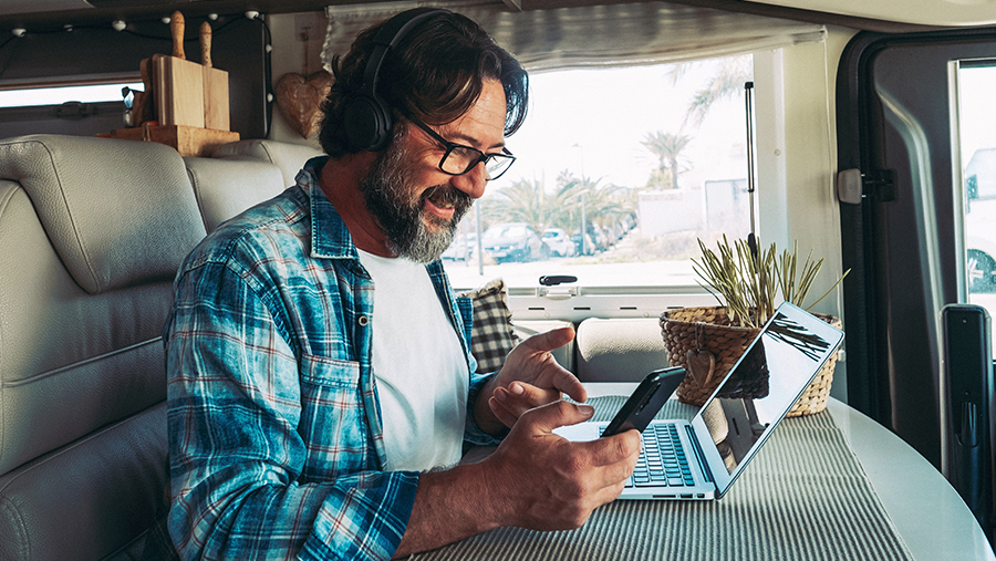 Man in RV doing work on cellphone and laptop