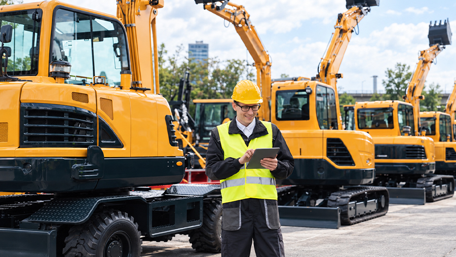 man with glasses smiling at tablet surrounded by excavators